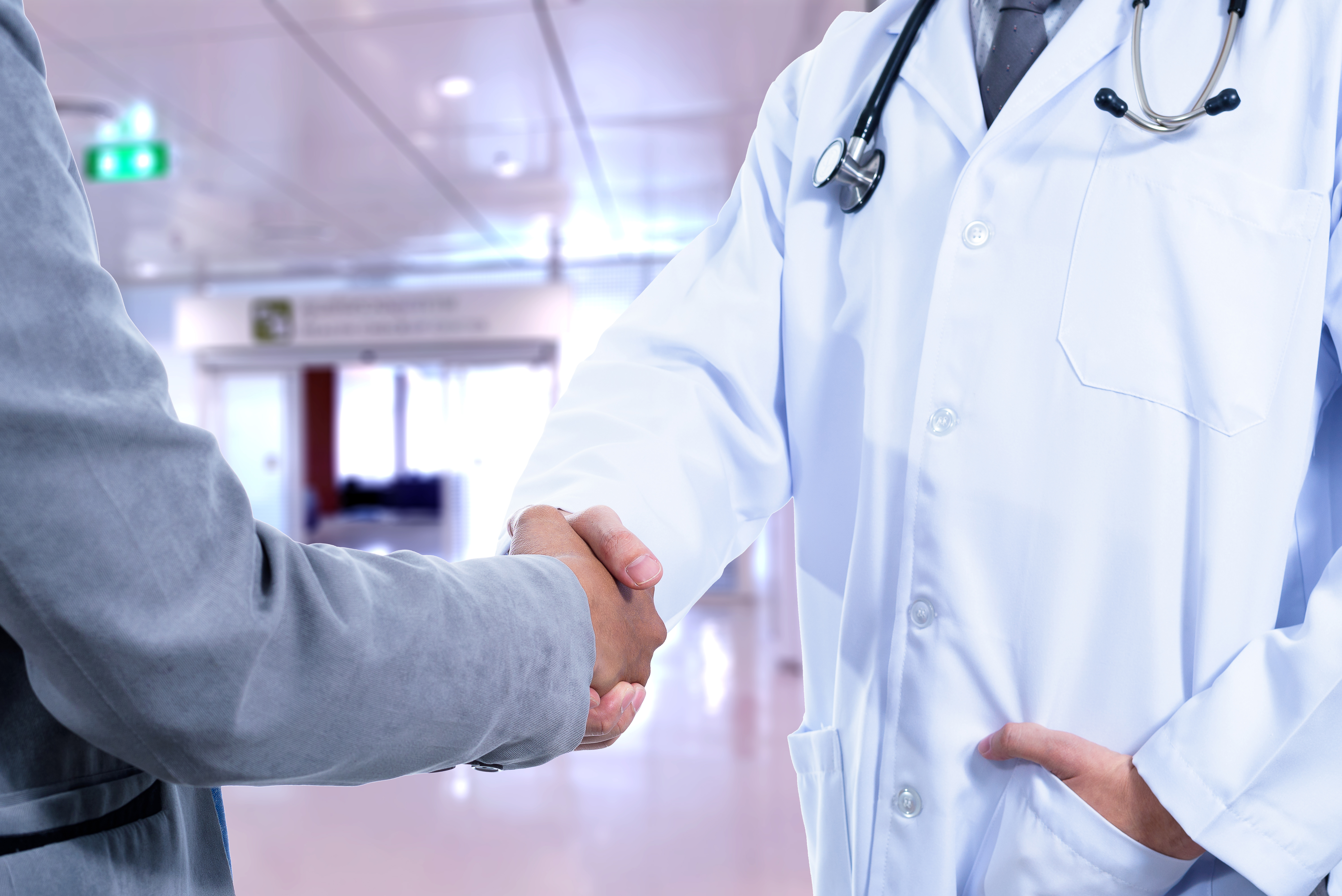 Doctor and Business man handshake with blurred hospital background
